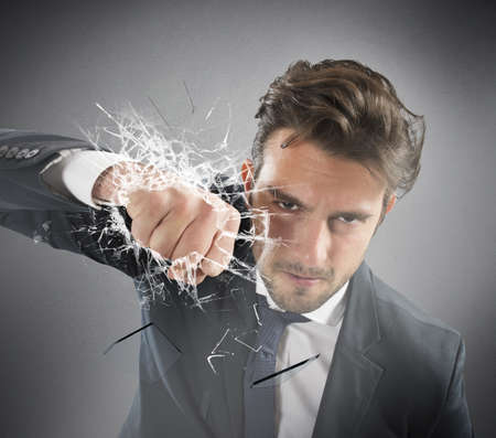 Determined businessman breaks the glass with punchの写真素材