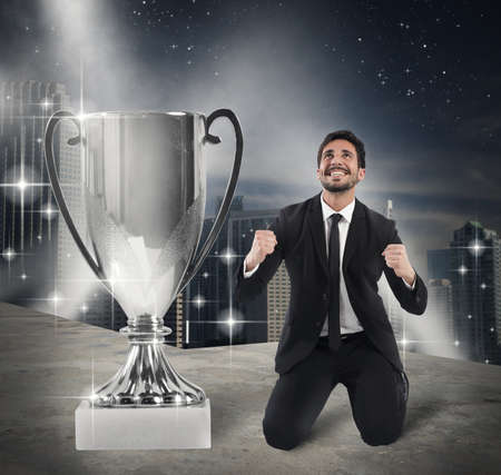 Businessman kneeling exult in front of cupの写真素材