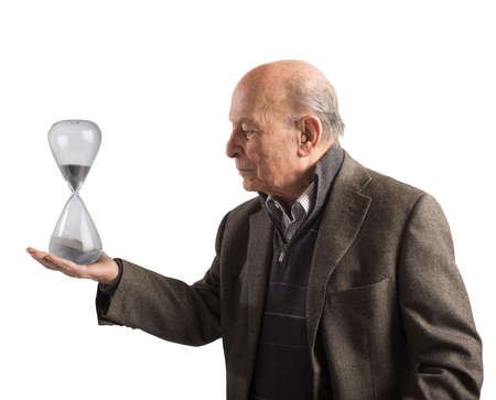 Elderly man holds an hourglass in handの写真素材