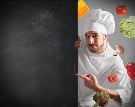 Smiling chef with blackboard and vegetables backgroundの写真素材