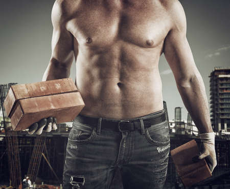 Sexy dirty bricklayer with brick in handの写真素材