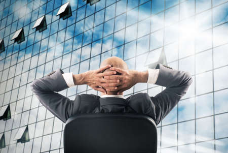 Man sitting relaxed watching a mirrored skyscraperの写真素材