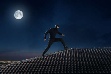 Thief dressed in black walking on the roof of a houseの写真素材