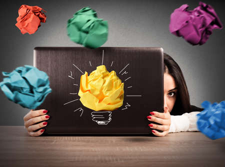 Businesswoman is protected behind the computer screen from paper balls