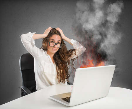 Businesswoman with stressed expression looks at the laptop on fireの写真素材