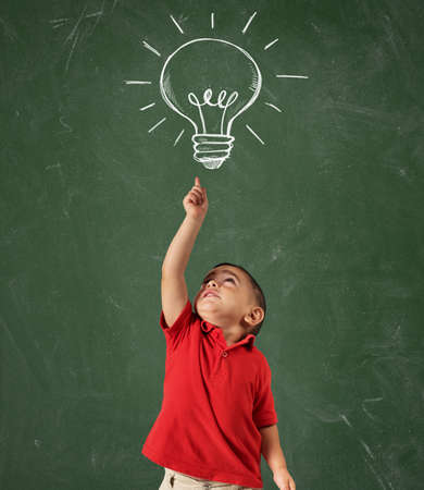 Child points a lightbulb drawn above his head on blackboard