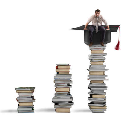 Businessman sitting on a pile of books with graduation capの写真素材