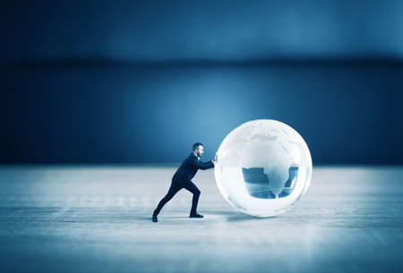 Businessman push a world glass sphere with continents on the tableの写真素材
