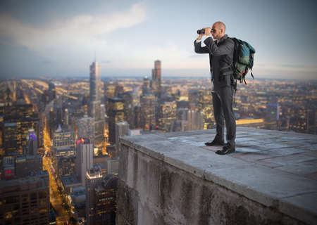 Businessman with backpack and binoculars watching from above the cityの写真素材