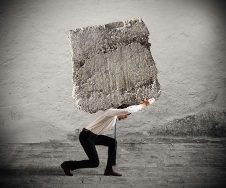 Businessman walking with a heavy boulder on his backの写真素材