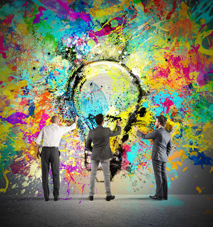 Business person paint together a big colored lightbulb on the wallの写真素材