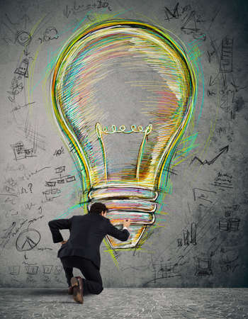Businessman draws on the wall a big colored bulb with bright colors and business sketchesの写真素材