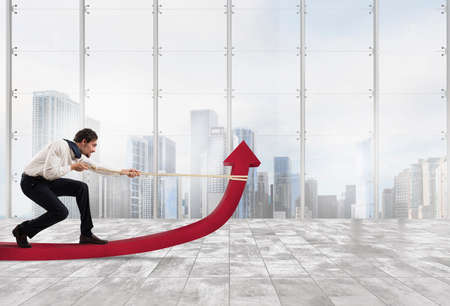 Determinated businessman with much effort lifts statistics arrow with a rope in a officeの写真素材