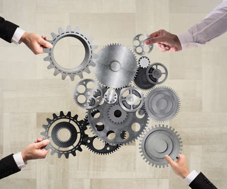 Teamwork of businesspeople work together and combine pieces of gears to a mechanical systemの写真素材