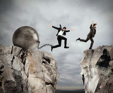 Man jumps between two mountains before the man with a heavy ball obstacleの写真素材