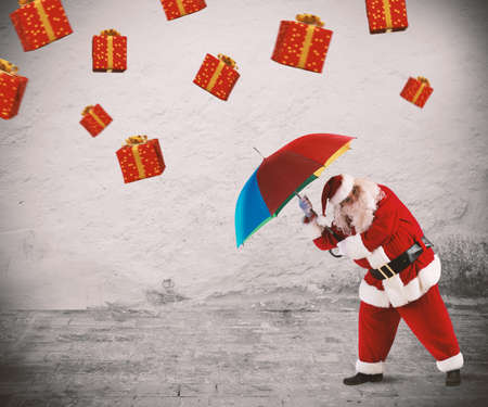 Santa claus is protected by gifts with umbrellaの写真素材