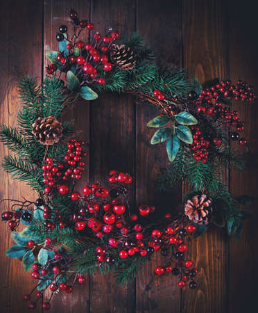 Christmas wreath decoration with pine cones and hawthorn berries on wooden backgroundの写真素材