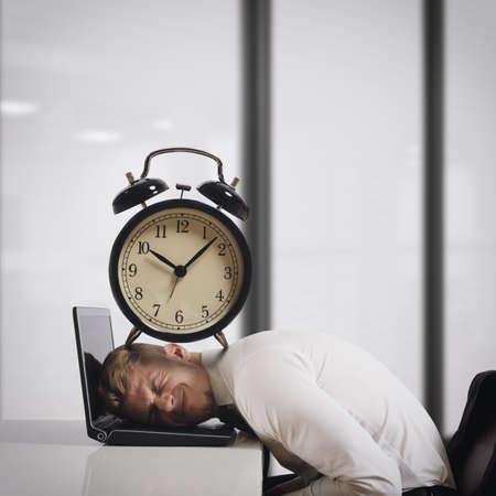 Businessman on laptop with a big alarm clock on head. Oppressed by deadlines concept