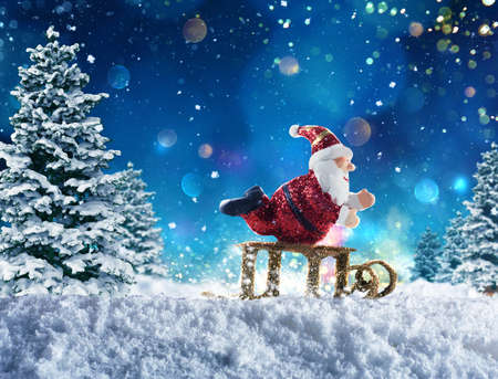Cute puppet of Santa Claus plays with sleigh on the snow