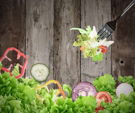 Background of mixed salad eaten with a fork on wooden boards. Healthy food for wellness conceptの写真素材