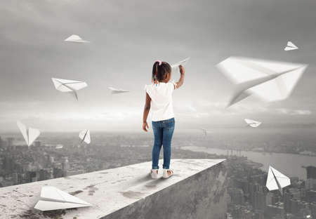 Little girl throws paper airplanes from a roof over the cityの写真素材