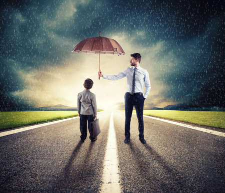 Businessman with umbrella that protect a child. Concept of young economy and startup protectionの写真素材