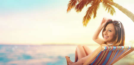 Beautiful girl sitting on a deck chair at the beach at sunset