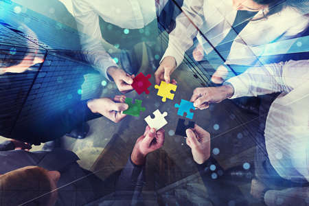 Business people join puzzle pieces in office. Concept of teamwork and partnership. double exposure with light effectsの写真素材