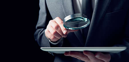 Businessman examines a tablet with a magnifying glass. Concept of internet security