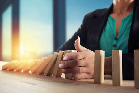 Businesswoman stops a chain fall like domino game. Concept of preventing crisis and failure in...