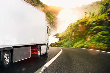 White truck moving on the road in a natural landscape at sunset
