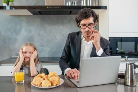 Annoyed daughter with her father that works with a laptopの写真素材