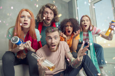 Happy friends of football fans watching soccer on tv and celebrating victory with falling confetti.