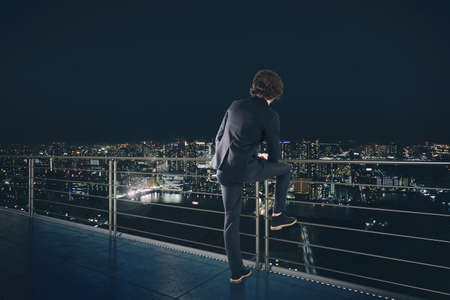 Businessman looks at the city during night. Future and new business opportunity conceptの写真素材