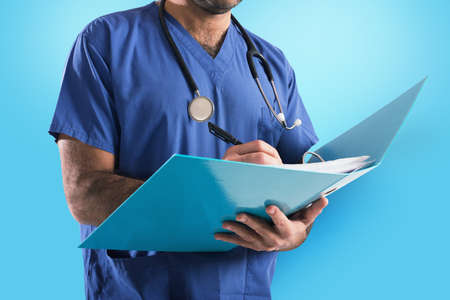 Doctor with stethoscope writes on medical recordの写真素材