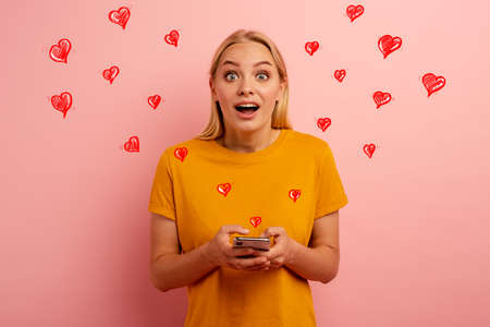 Blonde cute girl receives hearts on her smartphone.の写真素材