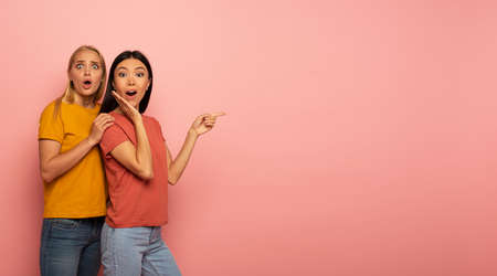 Two girls indicates something. Amazed expression face. Pink background with blank space for your...