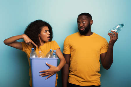Happy couple hold a plastic container with bottles over a light blue color. Concept of ecology,...