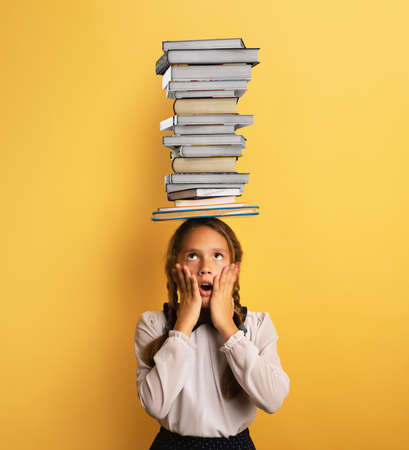 Young child student worried due to too much books to read and study. Yellow backgroundの写真素材