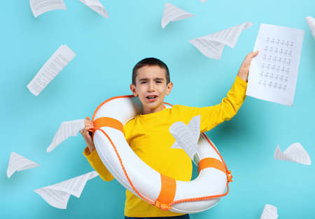 Young boy student is drowning in a sea of sheets of exercises.の写真素材