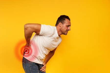 Aching man with back pain. Yellow backgroundの写真素材