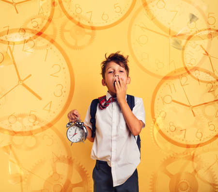 Young child student with ringing alarm clock is lazy going to school. Yellow background.の写真素材
