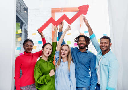 Young happy and colorful business team hold a red statistical arrow. Concept of growing, succesful and profitの写真素材