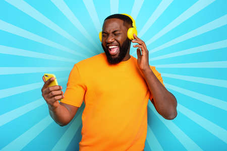 Boy with yellow headset listens to music and dances on cyan background. emotional and energetic expressionの写真素材