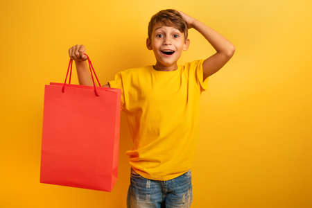Happy child are amazed about a shop sales. surprised, expression. Yellow background colorの写真素材
