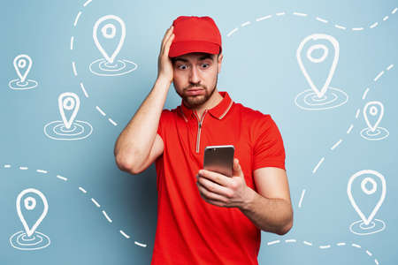 Confused courier man watches his smartphone due to a lot of packages to delivery