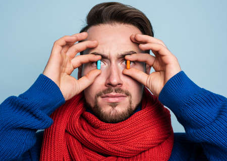 Boy caught a cold and uses pills to heal. Studio on Cyan background