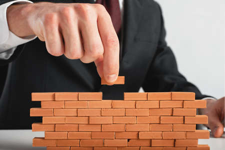Businessman puts a brick to build a big wall. Concept of new business, partnership, integration and startupの写真素材