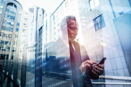 Busy senior business man uses mobile phone to communicateの写真素材