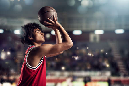 Basketball player throws the ball in the basket in the stadium full of spectatorsの写真素材